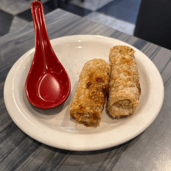 Two crispy Vietnamese egg rolls and a red spoon on a white plate at Pho Saigon Basil.
