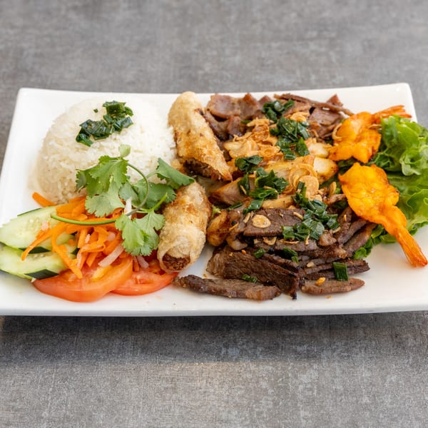 A Vietnamese platter with rice, spring rolls, grilled beef, shrimp, and fresh vegetables.