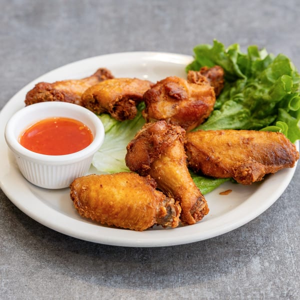 Crispy fried chicken wings with lettuce and a side of sweet chili sauce on a white plate.