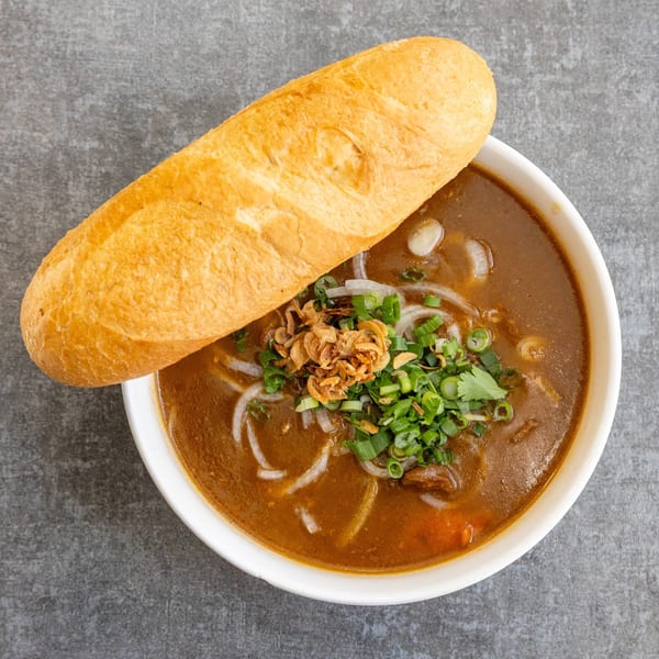 A bowl of Vietnamese Pho Saigon Basil with a baguette on the side, garnished with herbs.