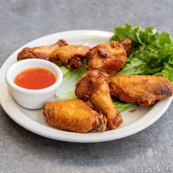 Crispy fried chicken wings with a side of sweet chili sauce and lettuce on a white plate.