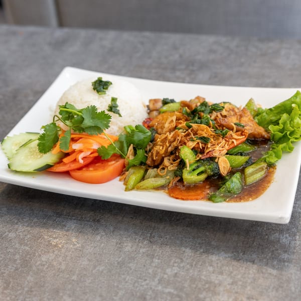Vietnamese stir-fried chicken with broccoli, carrots, and fried onions, served with rice and fresh vegetables.