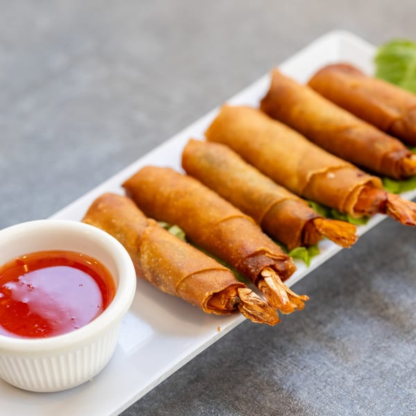 Five crispy Vietnamese shrimp spring rolls with sweet chili dipping sauce on a white plate.
