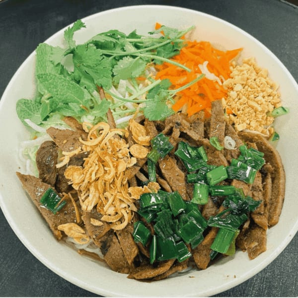 A Vietnamese vermicelli bowl with sliced meat, fried onions, green onions, carrots, and herbs.