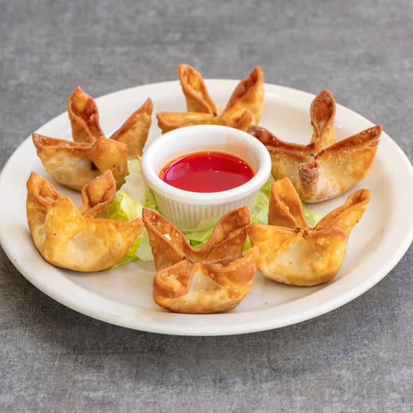 Crispy golden crab rangoons arranged on a white plate with a side of sweet chili sauce.