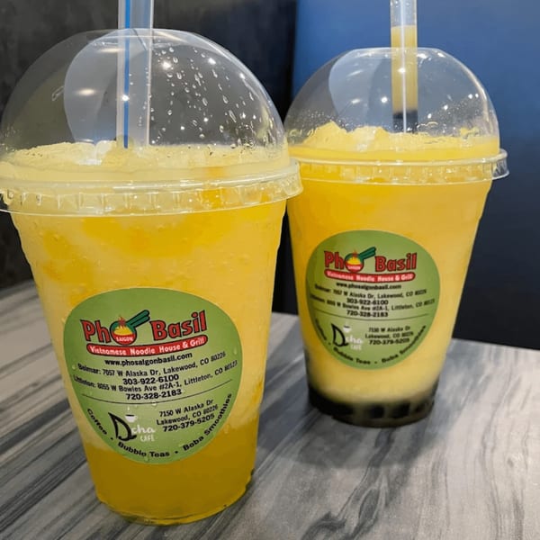 Two Pho Saigon Basil mango smoothies with straws and green labels on a table.
