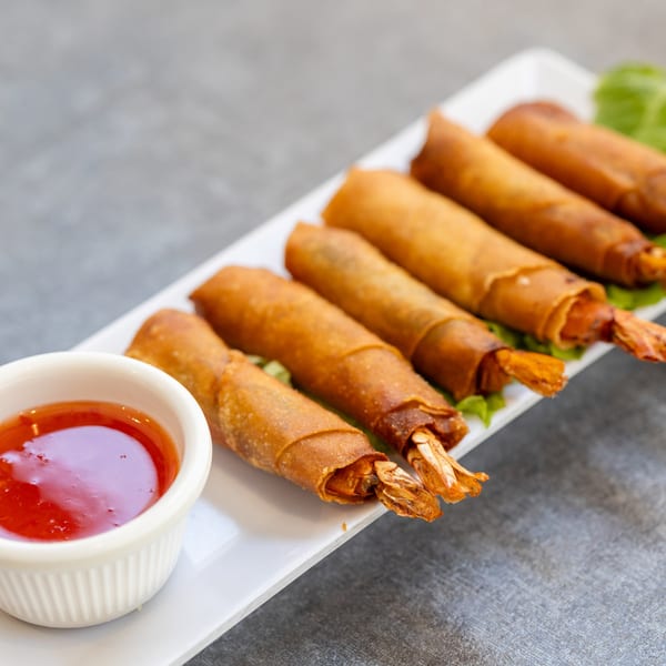 Crispy Vietnamese shrimp spring rolls with sweet chili dipping sauce on a white rectangular plate.