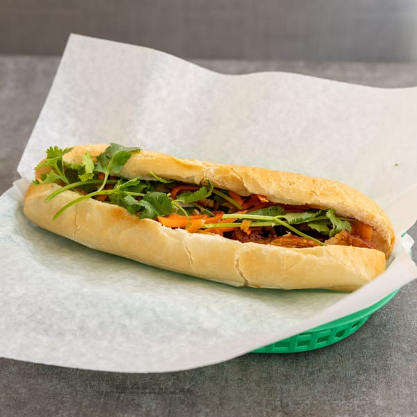 A Vietnamese Banh Mi sandwich with cilantro and carrots in a green basket.