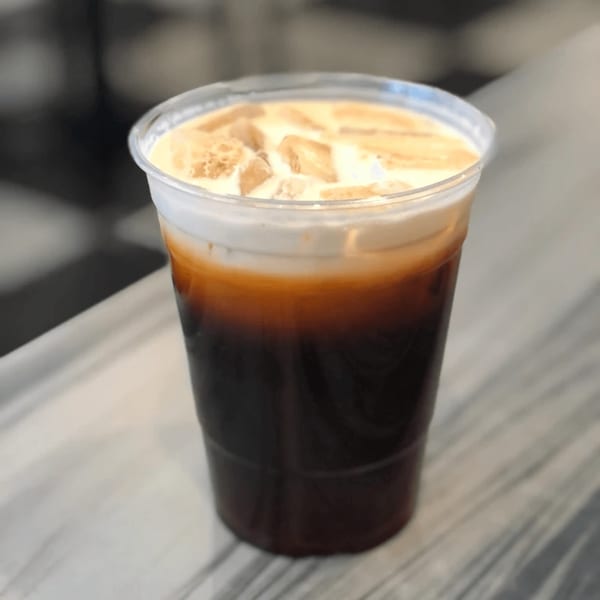 Iced Vietnamese coffee with a creamy foam topping and ice cubes in a clear plastic cup.