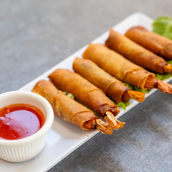 Crispy Vietnamese shrimp spring rolls with sweet chili dipping sauce on a white rectangular plate.