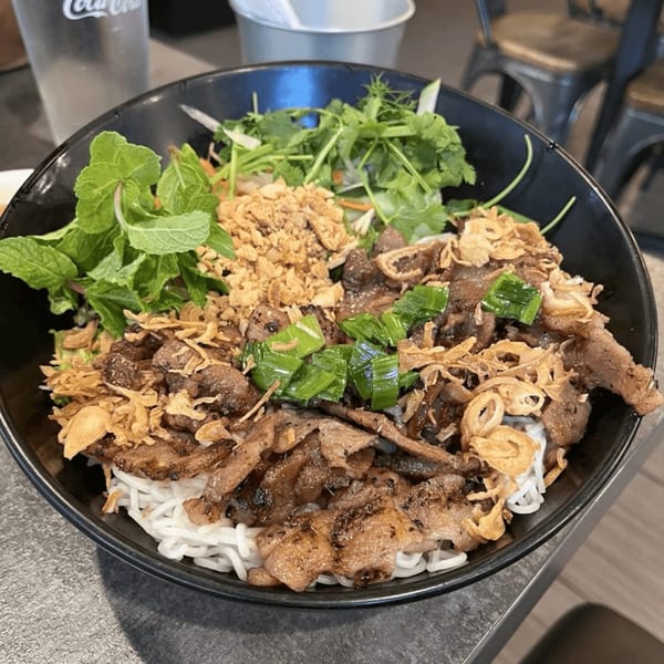 A large bowl of Vietnamese vermicelli noodles with grilled pork, fresh herbs, and crispy fried shallots.