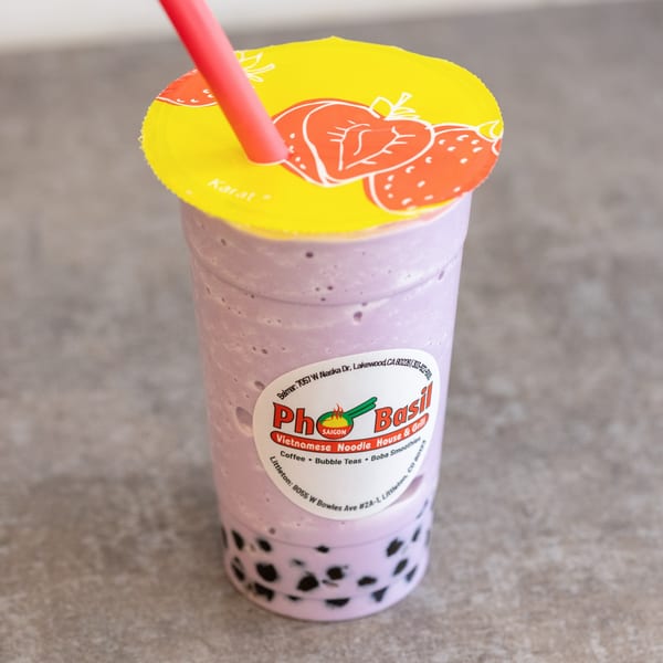 A Pho Saigon Basil taro boba smoothie with a red straw and strawberry-patterned lid.